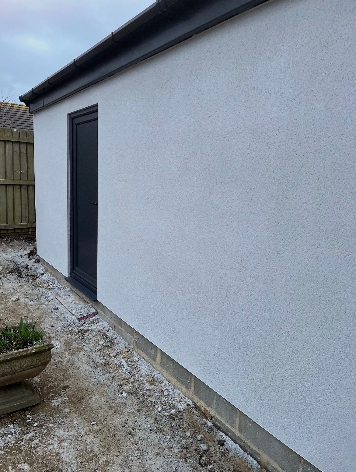 Freshly rendered outbuilding with a dark grey door and new guttering
