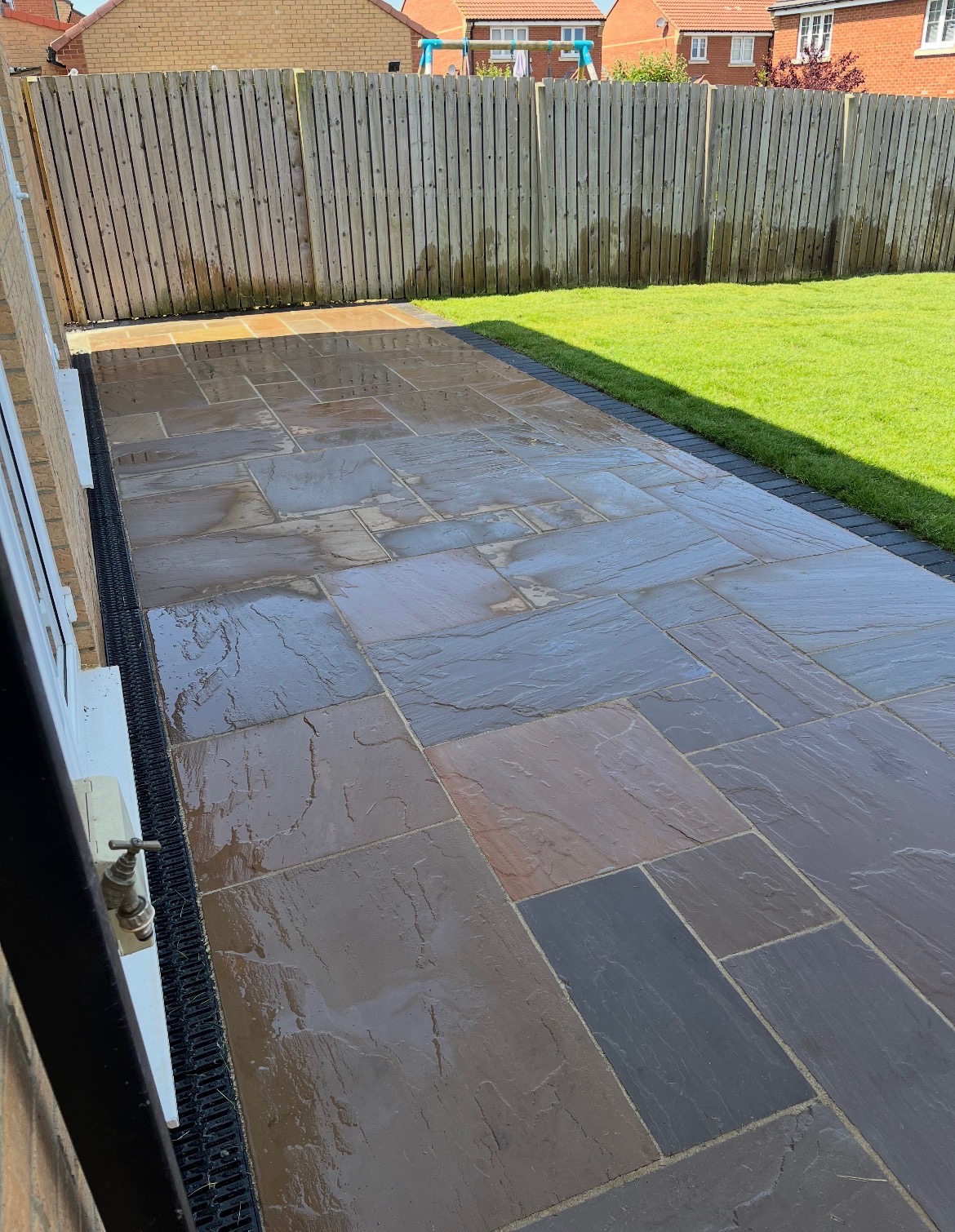 Newly laid sandstone flagstone patio with dark edging beside a house